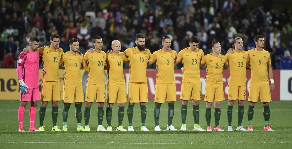 Los jugadores de la selección de fútbol de Australia guardan un minuto de silencio mientras los de Arabia Saudí corretean en su campo.