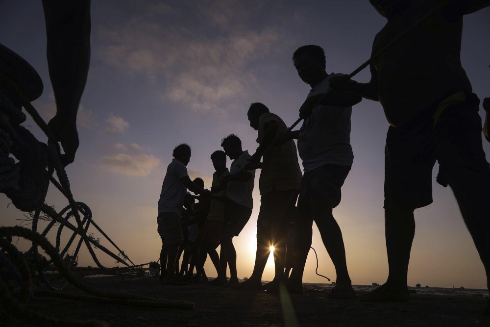 Varios pescadores preparan su captura durante la puesta de sol.