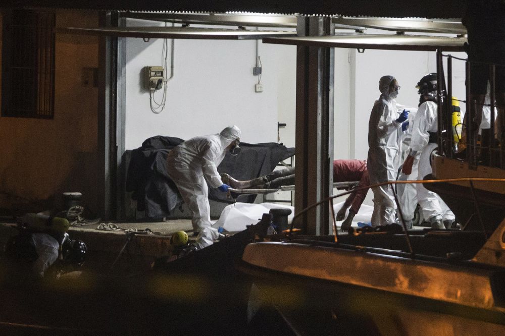 Bomberos y agentes de la Guardia Civil trasladan los cuerpos de los 5 inmigrantes fallecidos que viajaban en una patera avistada ayer en alta mar por un buque mercante maltés y que ha llegado de madrugada al puerto de Cartagena.