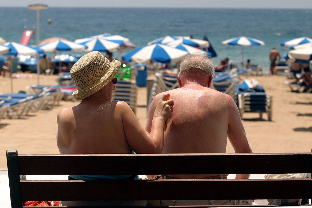 Una pareja de turistas se da crema solar junto a la playa de Benidorm.