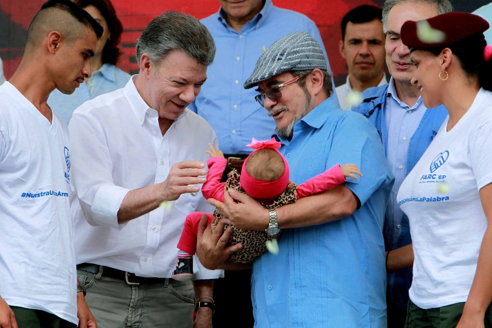 El presidente de Colombia, Juan Manuel Santos (c-i), saluda a una bebé que es sostenida por el máximo líder de las FARC, Rodrigo Londoño, alias "Timochenko", durante la ceremonia de dejación de armas hoy, martes 27 de junio.