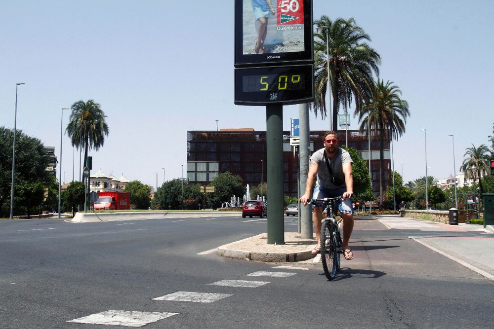 Un joven pasa con su bicicleta junto a un termómetro que marca 50 grados hoy en una calle de Córdoba.