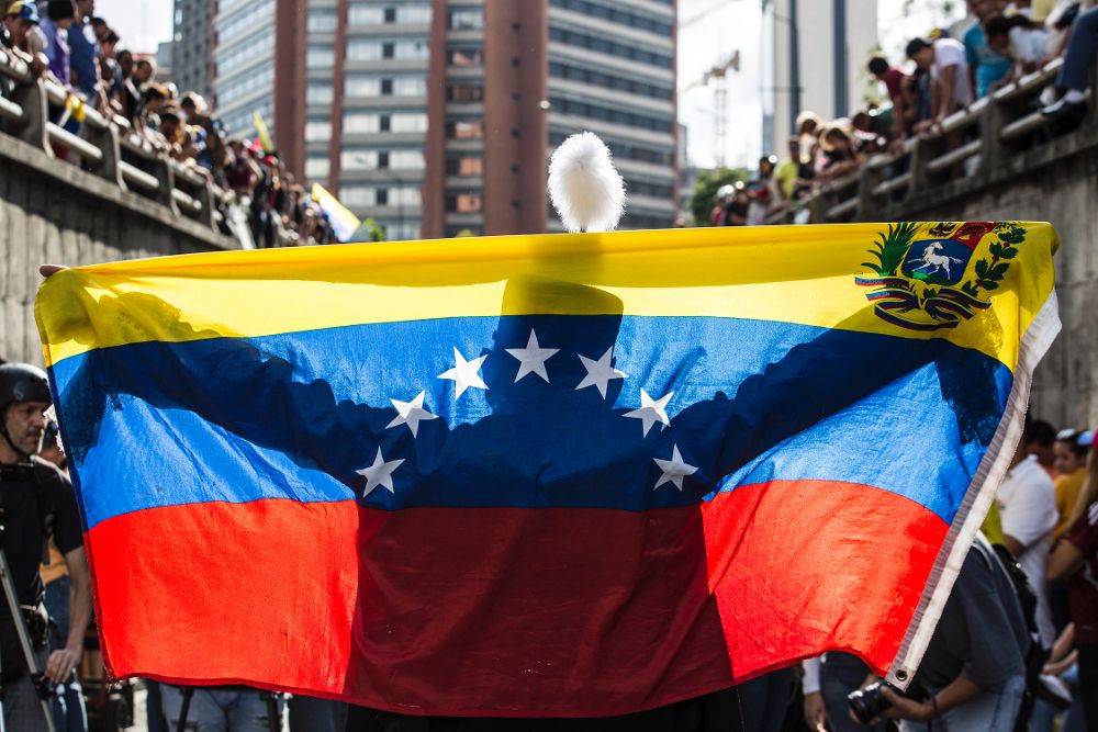 Una persona extiende una bandera venezolana ante decenas de manifestantes durante una protesta antigubernamental de ayer, lunes, en Caracas.