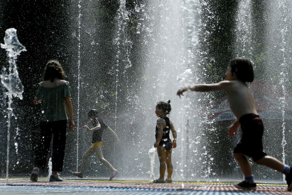 Varios niños corren bajo el agua de una fuente para combatir el calor.