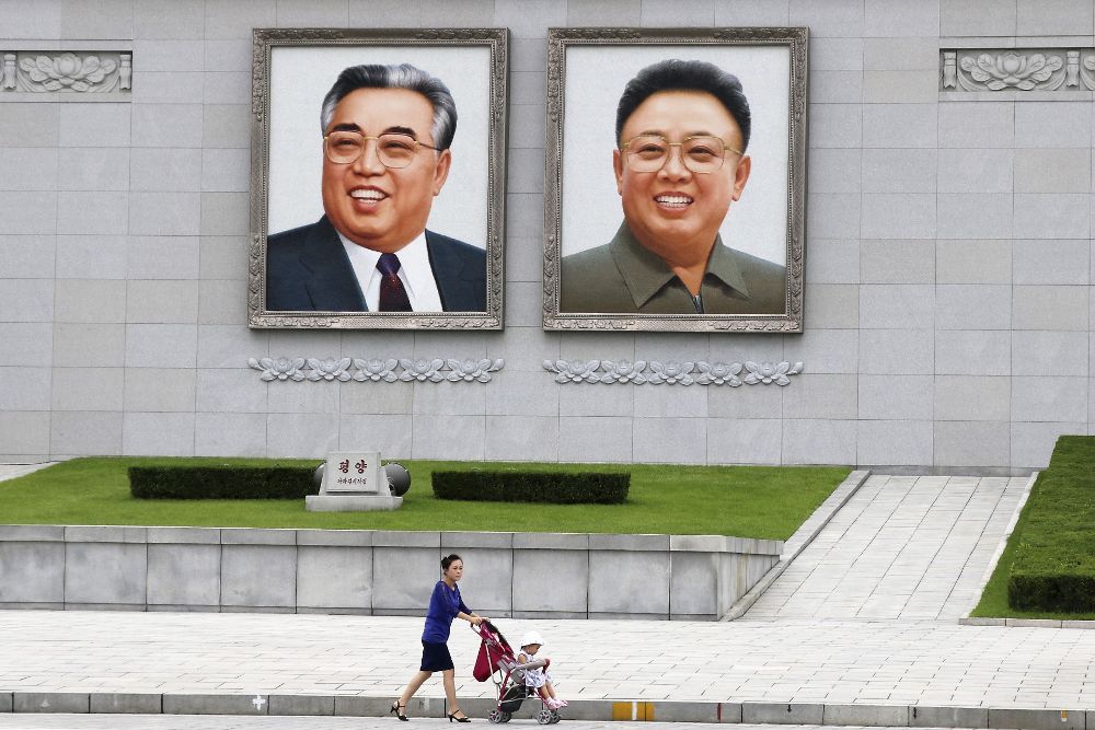 Un mujer con un carrito de niños pasa delante de los retratos de los líderes Kim il sung y Kim Jong il en la plaza Kim il Sung de Pyongyang.