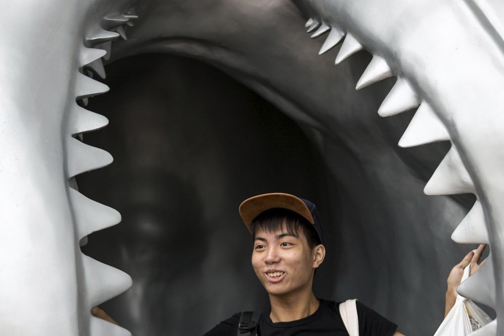 Un hombe posa junto a una escultura de la boca de un tiburón gigante.
