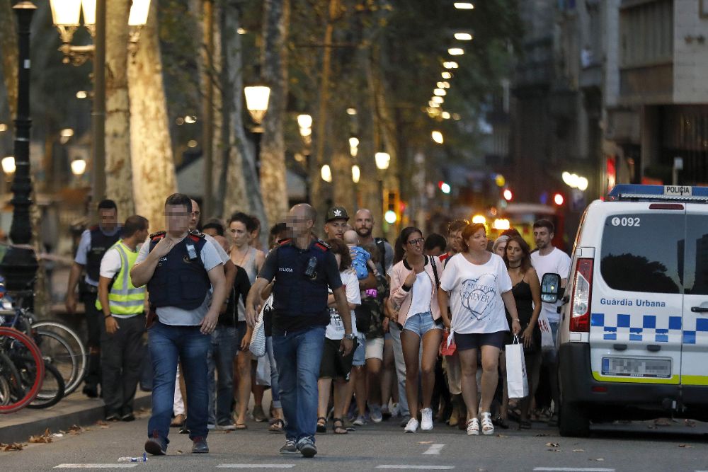 Un grupo de gente se desplaza esta noche entre el despliegue policial en el lugar del atentado ocurrido por la tarde en las Ramblas de Barcelona.