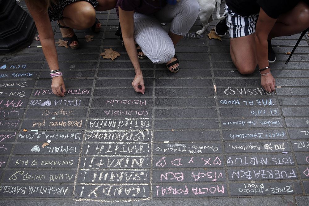 Varias personas escriben con tiza mensajes de apoyo en una acera de Las Ramblas de Barcelona.