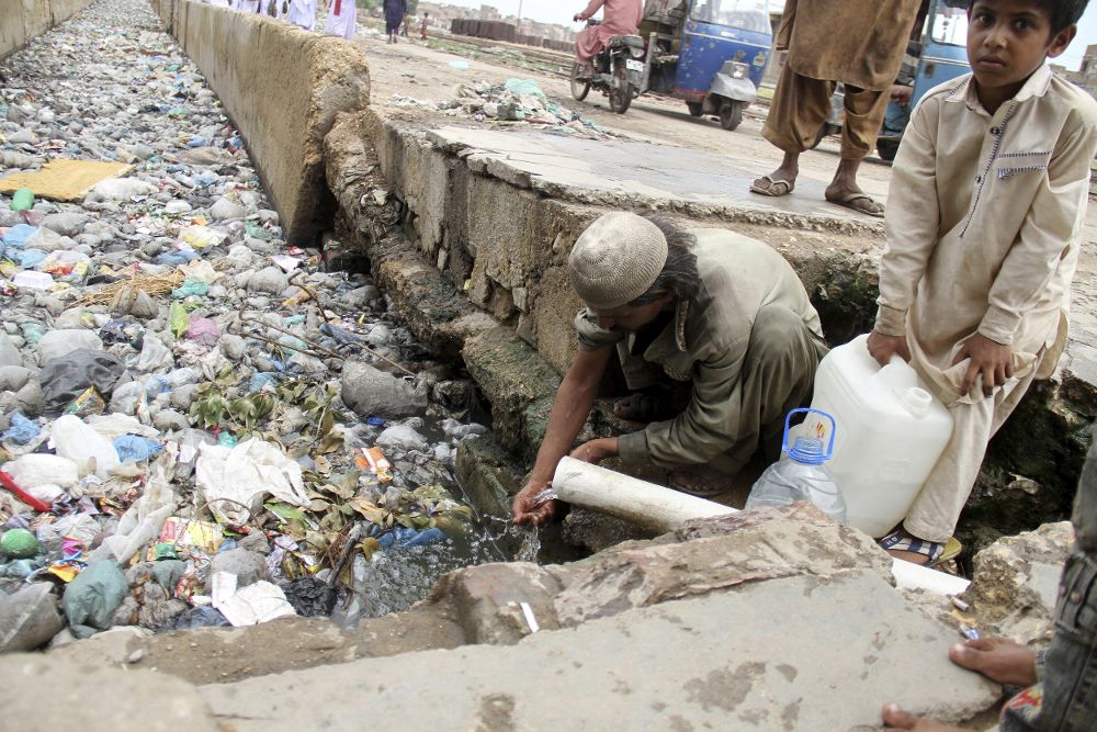 Varias personas recogen agua de una tubería sobre una línea de aguas residuales en Hyderabad (Pakistán).