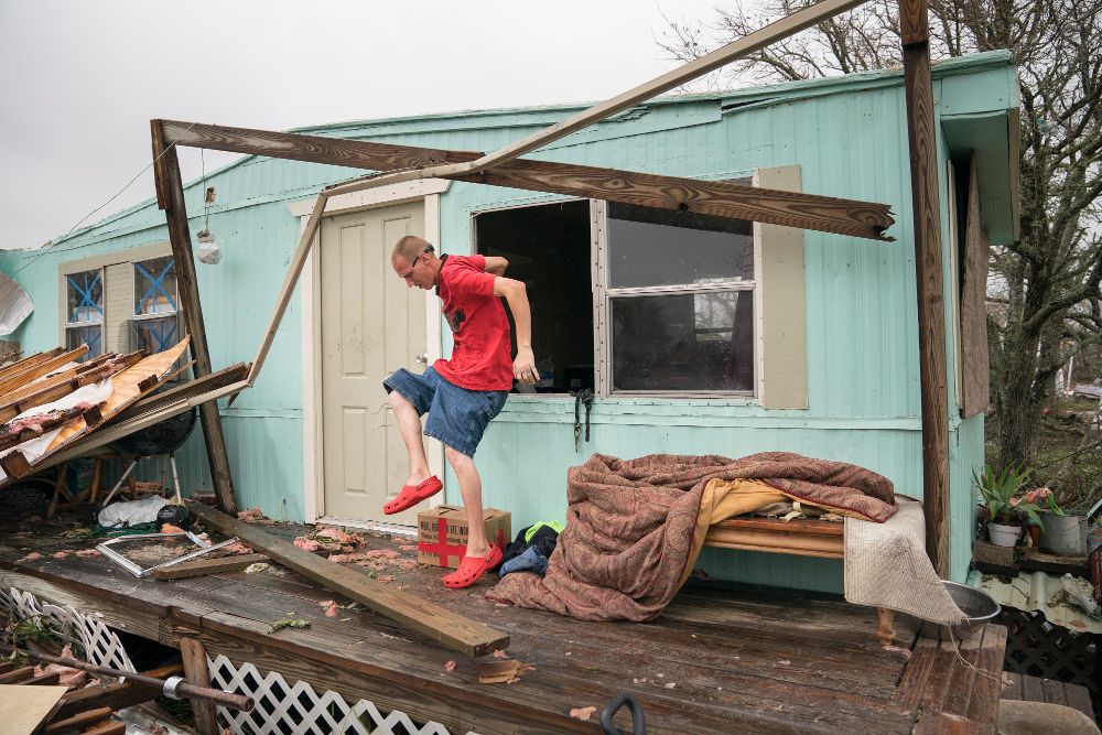 Un hombre salta desde la ventana de su casa mientras busca sus pertenencias tras el paso del Huracán Harvey en Rockport, Texas.