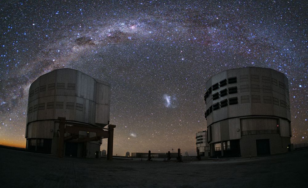 Vista del cielo desde el Observatorio Paranal (Chile). Recorriendo la parte superior de la imagen se observa el plano de nuestra galaxia, la Vía Láctea. En el centro, entre los dos telescopios, se ven la Gran Nube (galaxia superior) y la Pequeña Nube de Magallanes (abajo a la izquierda). ESOYuri Beletsky 