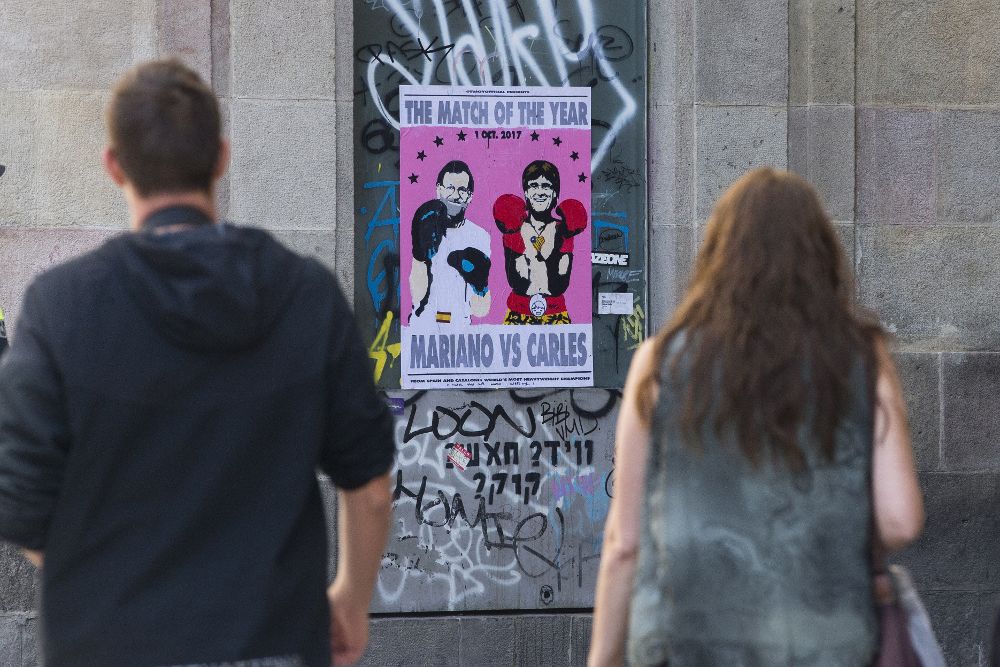 Varias personas pasan por delante de un cartel alegórico a la situación catalana.