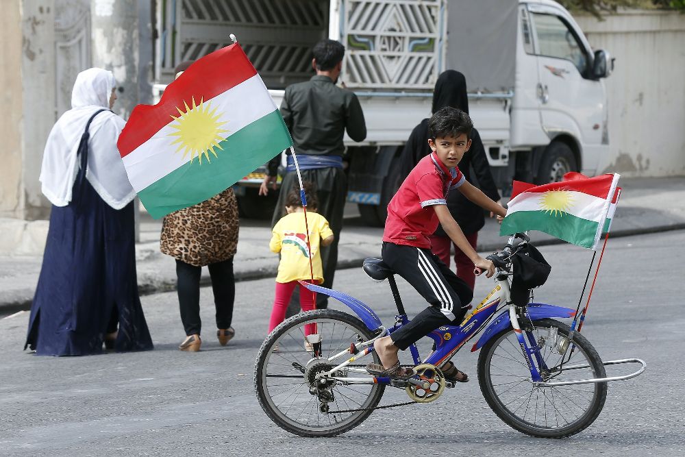 Un niño kurdo monta en una bici decorada con banderas kurdas.