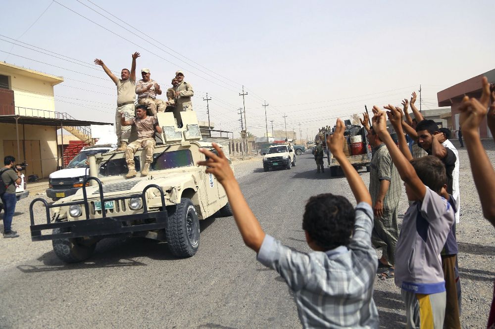 Civiles iraquíes saludan a un convoy militar.
