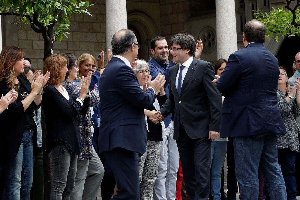 El presidente catalán, Carles Puigdemont (c), junto al vicepresidente Oriol Junqueras (d), y el conseller de Presidencia, Jordi Turull (i), saluda a los trabajadores de la Generalitat que les han recibido con aplausos a su llegada a la reunión extraordinaria del gobierno catalán.