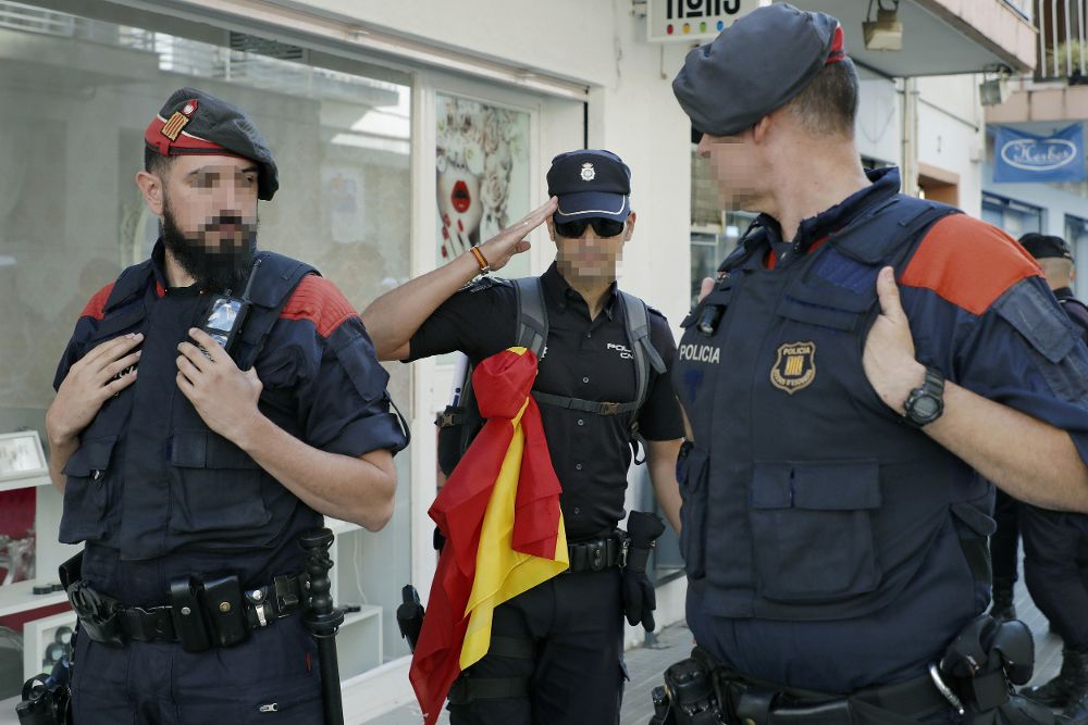Un policia nacional con la bandera española se despide de dos mossos de escuadra a su salida del hotel de Pineda de Mar.