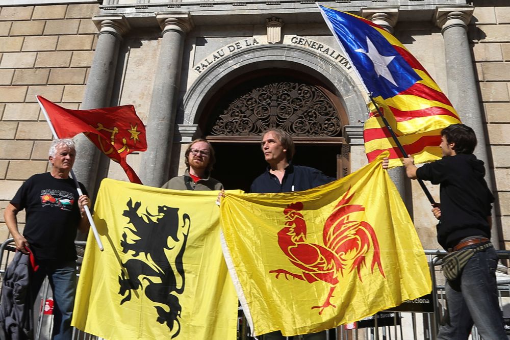 Cuatro personas sostienen las banderas (de izda a dcha) de las regiones de Occitania, Flandes, Valonia y la estelada, ante el Palau de la Generalitat, en el primer día laborable tras la puesta en marcha del artículo 155.