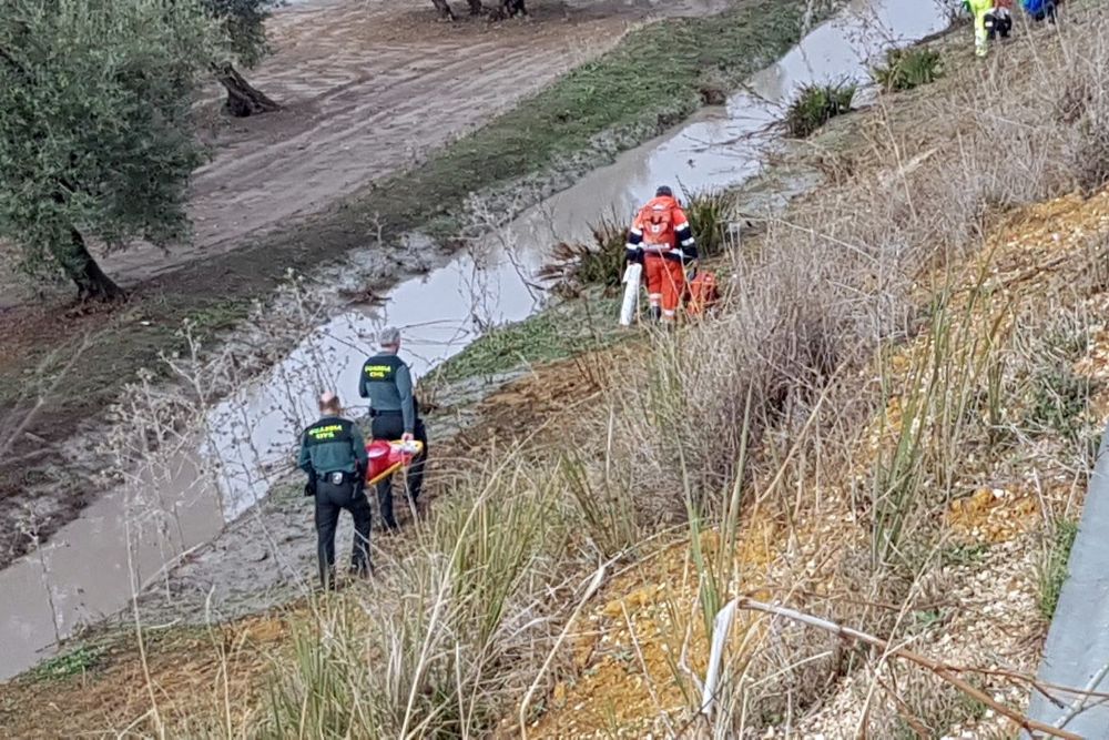 Agentes de la Guardia Civil y personal de los servicios de emergencias caminan por el terreno junto a la carretera inundada hacía el tren de pasajeros que descarriló.