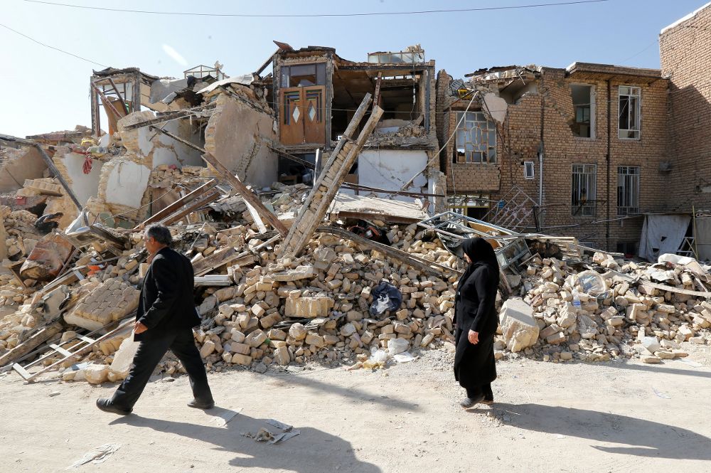 Dos residentes pasan delante una casa derrumbada en la localidad de Sare Pole-Zahab, provincia de Kermanshah (Irán) el pasado 16 de noviembre de 2017. 