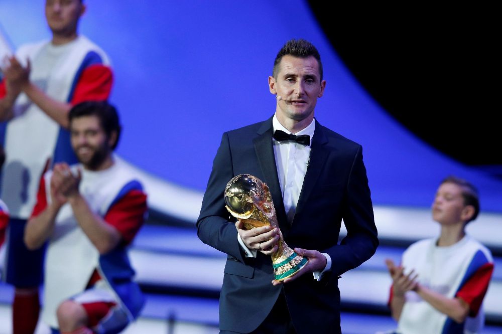 El exfutbolista alemán Miroslav Klose llega al escenario con el trofeo de campeón durante el sorteo del Mundial de Rusia 2018.