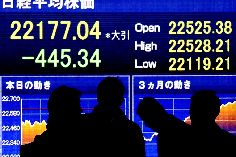 Varias personas pasan por delante de una pantalla con la información del cierre de la Bolsa de Tokio, en Japón, hoy 6 de diciembre.