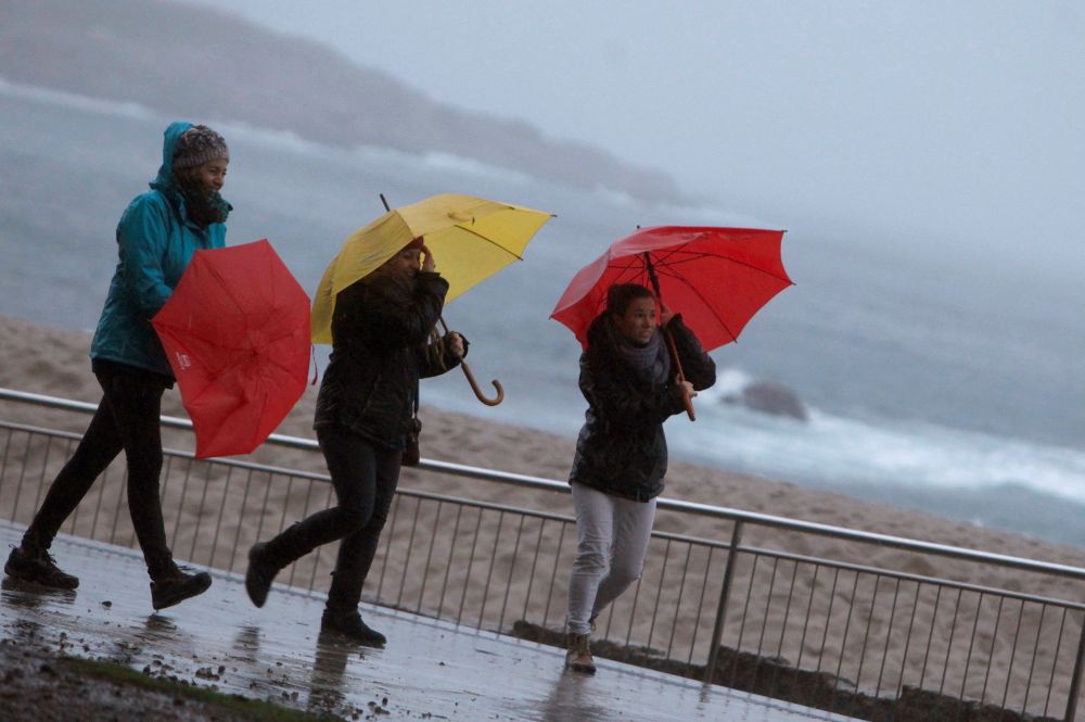 Tres mujeres se protegen de la lluvia en el paseo marítimo de A Coruña. 