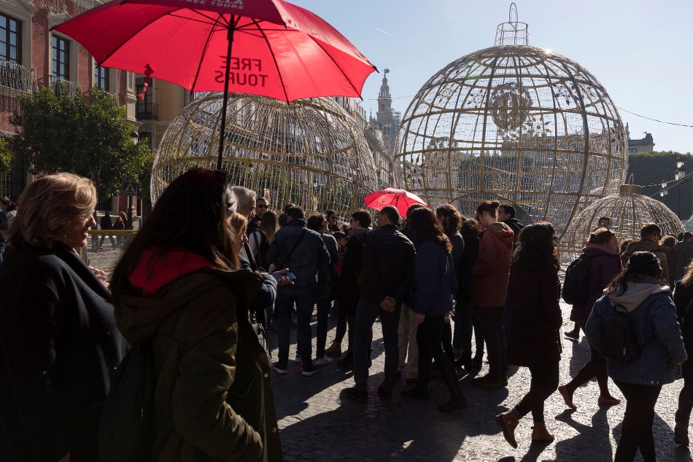 Grupos de turistas pasean ante los adornos navideños en el centro histórico de Sevilla durante el puente de la Constitución.