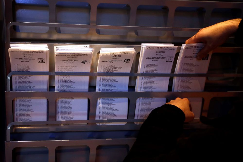Un operario coloca papeletas electorales en una cabina en el Ayuntamiento de Barcelona.