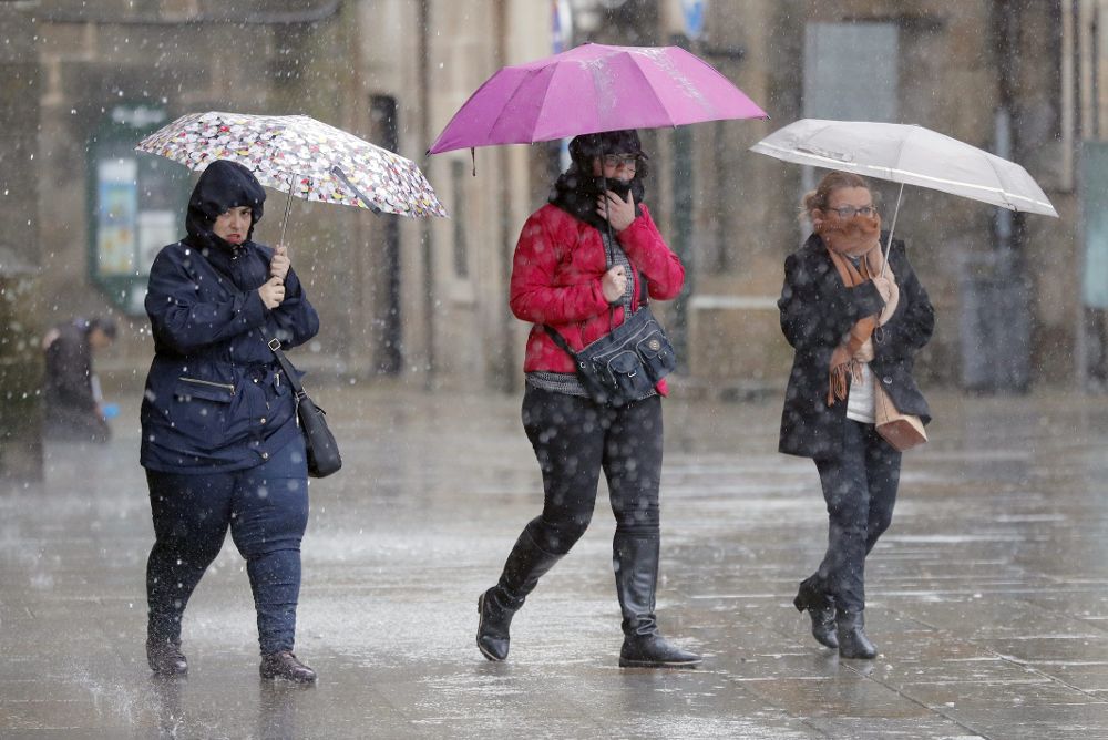 Varias personas transitan bajo la lluvia la plaza del Obradoiro, en Santiago de Compostela. 