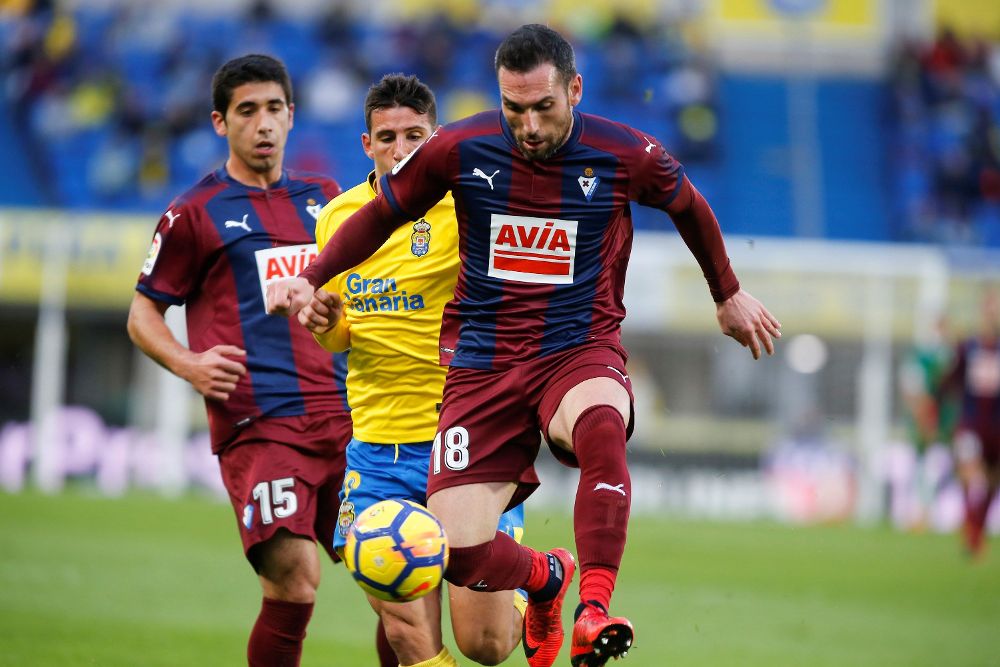 El delantero argentino de la Unión Deportiva Las Palmas Jonathan Calleri (c) pelea un balón contra los jugadores del Éibar José Ángel (i), y Anaitz Arbilla.
