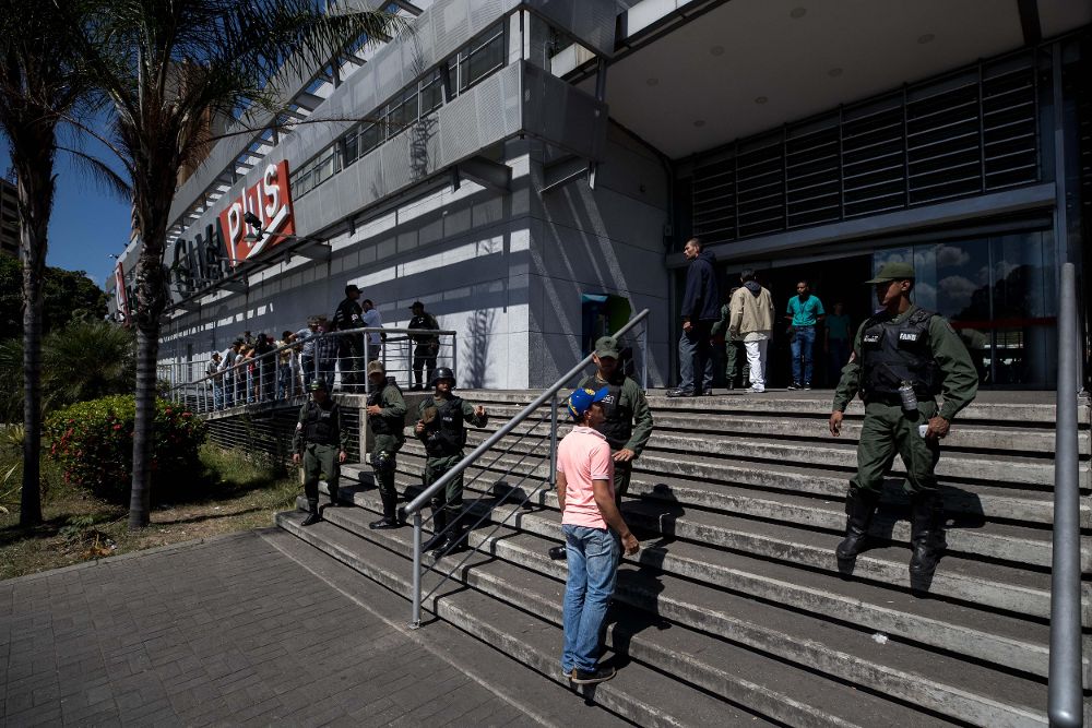 Personas hacen cola en la entrada de un supermercado de Caracas vigilado por soldados.