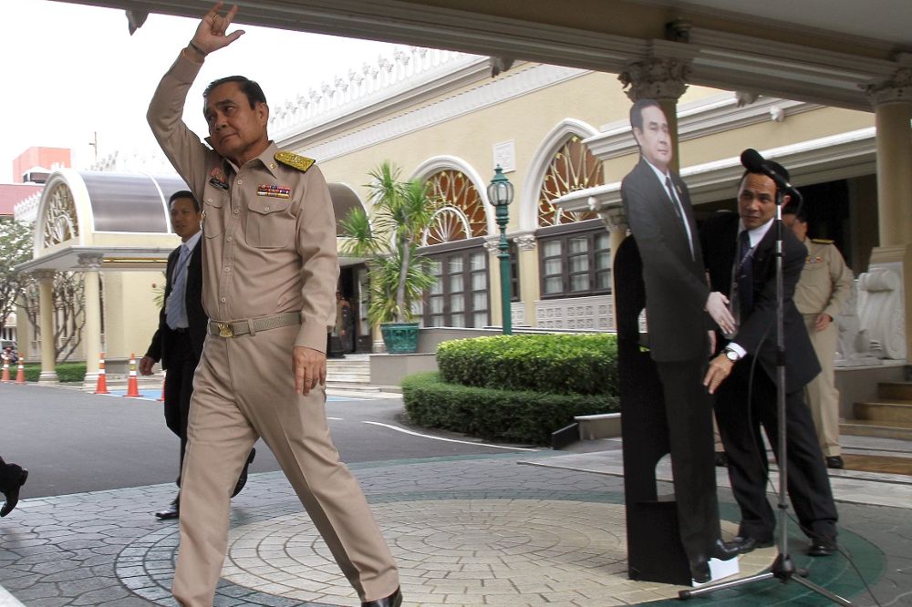 El primer ministro de Tailandia, Prayut Chan-o-cha, se despide de los periodistas con la seña "te quiero" del lenguaje de signos mientras deja una fotografía suya a tamaño real ante el micrófono.