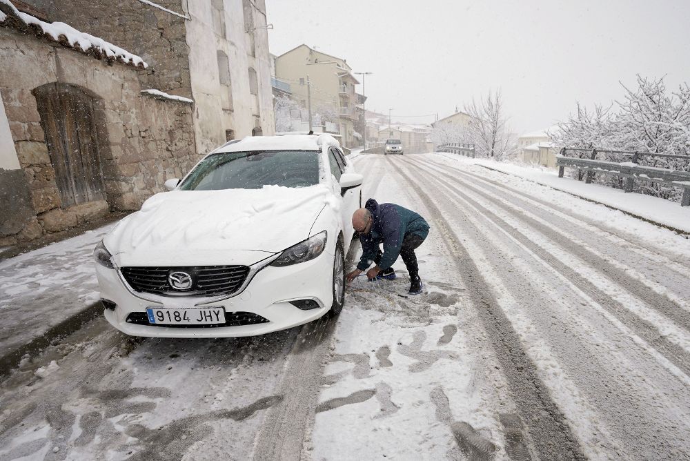 Un hombre pone cadenas a su coche en Cedrillas (Teruel) que se encuentra cubierta por la nieve caída en las últimas horas.