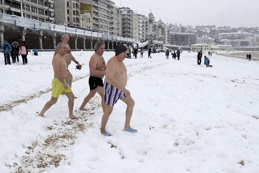 Un grupo de bañistas se dirigen al agua en la bahía de la Concha de San Sebastián, hoy, miércoles, en medio de la nieve.