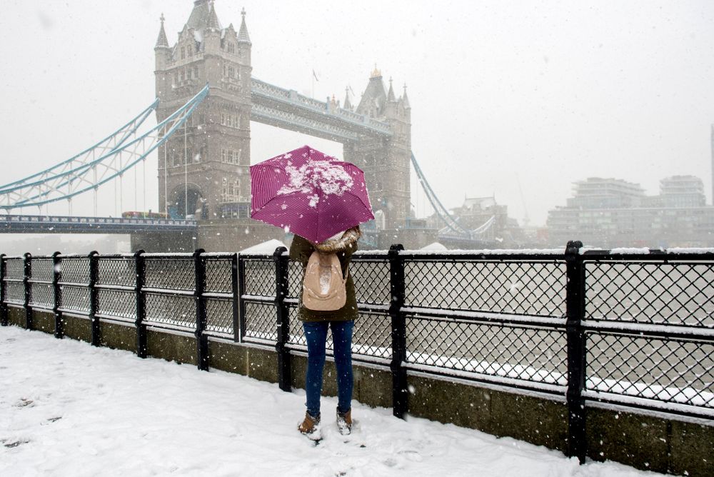Una turista permanece bajo una tormenta de nieve junto al Tower Bridge de Londres.