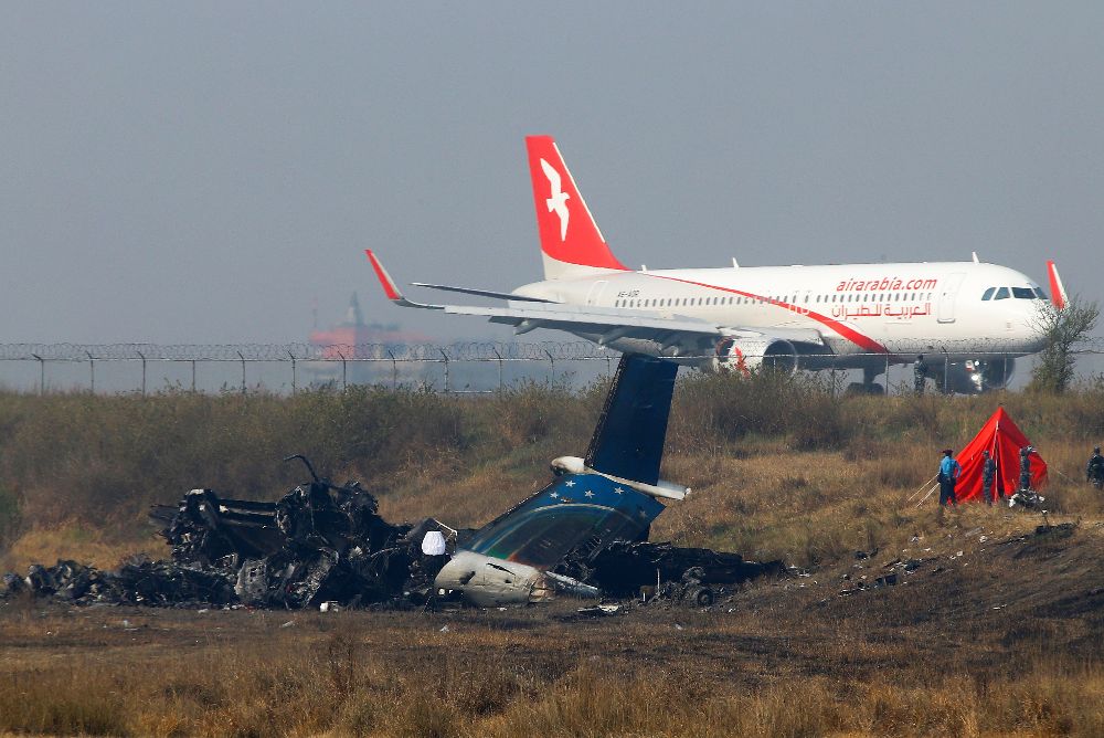 Un avión de Airarabia aterriza en el aeropuerto Tribhuvan en Katmandú cerca de los restos del avión que se estrelló el lunes en Katmandú.