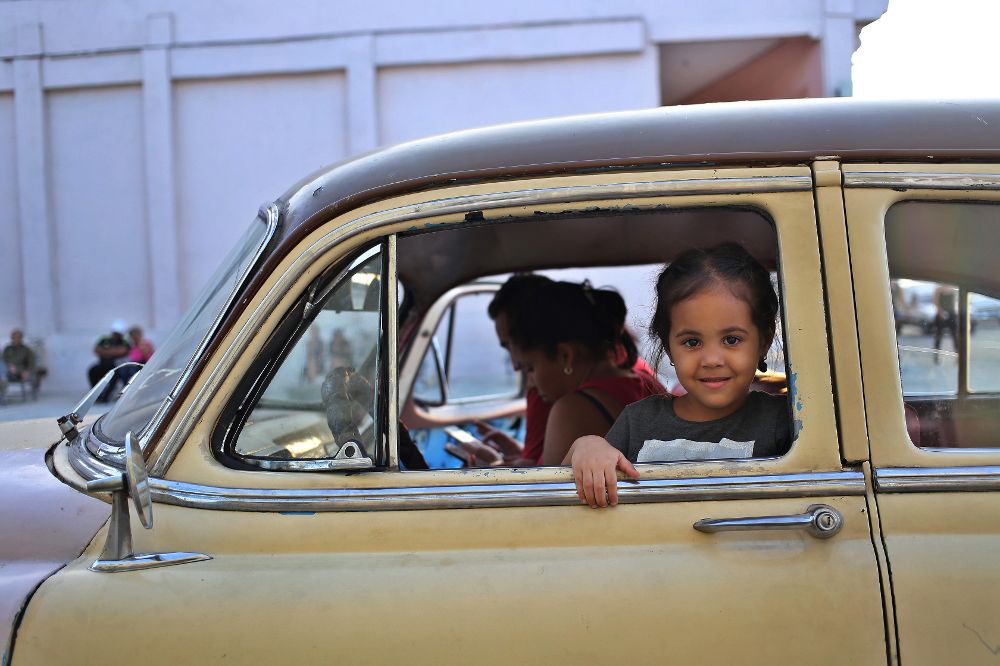 Una niña posa en la ventana de un viejo auto mientras sus padres se conectan a internet en una "zona WiFi".