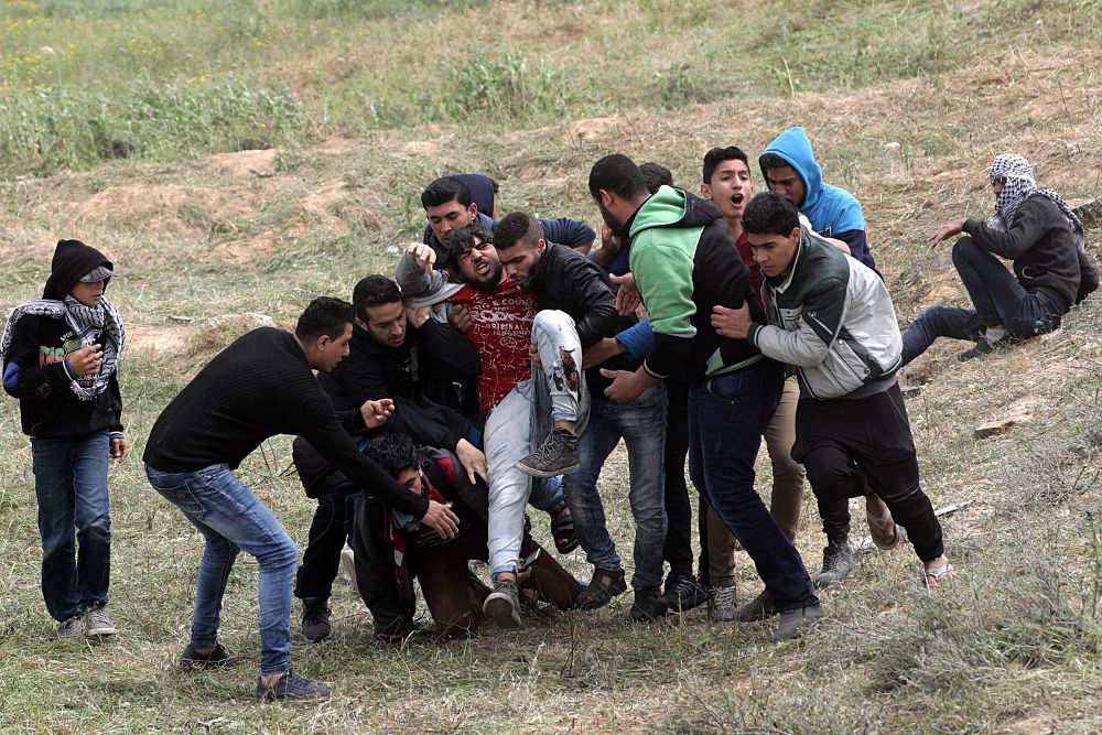 Varios palestinos ayudan a un compañero herido durante los enfrentamientos con soldados israelíes en el este de Beit Hanun, norte de la Franja de Gaza, el 30 de marzo del 2018. 