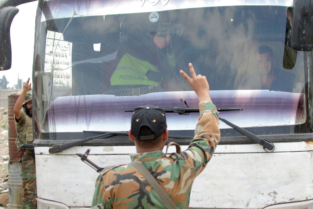 Soldados sirios hacen el símbolo de la victoria frente a un autobús que traslada a miembros del Ejército del Islam, en Duma, a las afueras de Damasco.