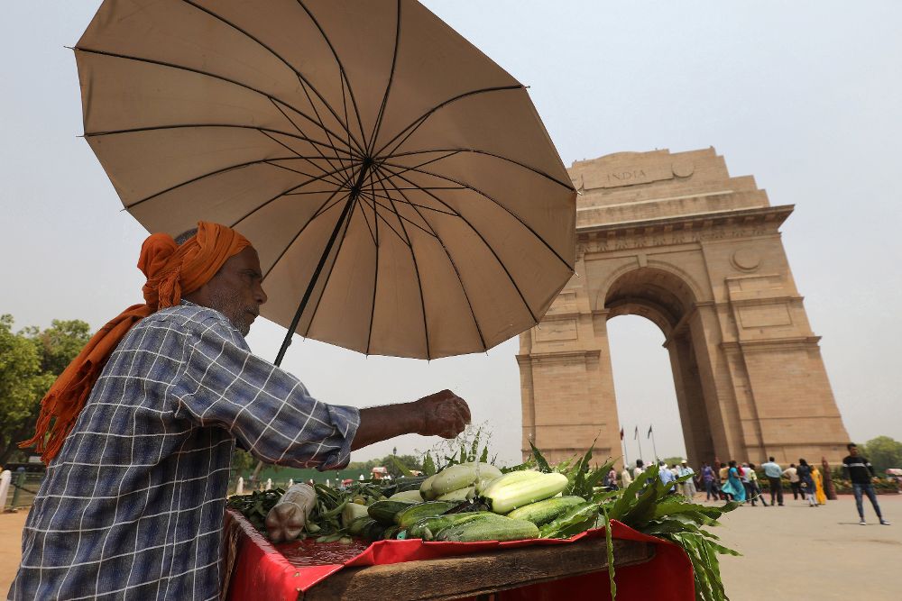 Un vendedor ambulante se protege del sol con un paraguas en una tarde calurosa en Nueva Delhi, India, hoy, 27 de abril de 2018.