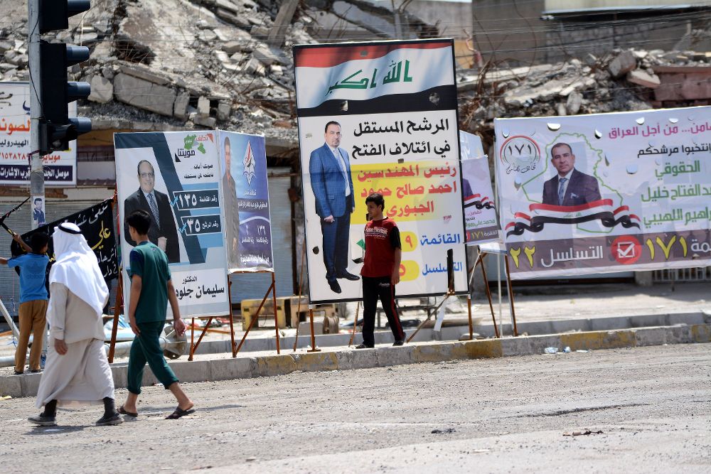 Varios ciudadanos de Mosul pasan al lado de los posters de la campaña electoral que vive Irak.