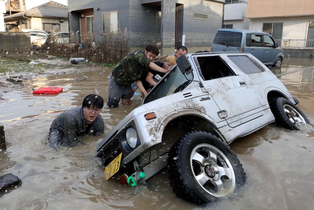 Varios vecinos tratan de levantar un vehículo cubierto por las aguas en Kurashiki, en la prefectura de Okayama.