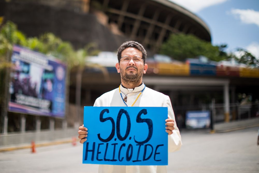 Un sacerdote sostiene un cartel en el que se lee "SOS Helicoide" frente al edificio "El Helicoide", sede del Servicio Bolivariano de Inteligencia Nacional (SEBIN). El motín iniciado este lunes por parte de un grupo de considerados "presos políticos" en los calabozos del Servicio de Inteligencia en Caracas se mantiene.