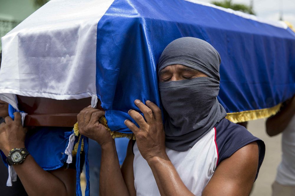 Un hombre con la cara tapada llora mientras carga el ataúd de José Medina, que falleció el pasado fin de semana durante un enfrentamiento entre parapoliciales y manifestantes.