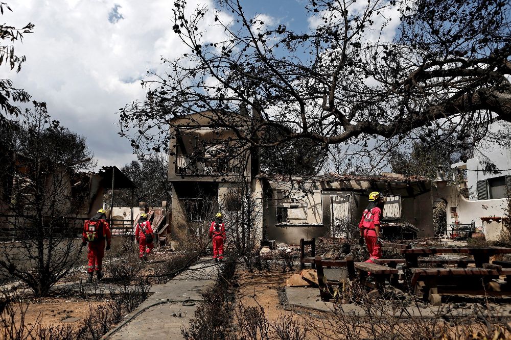 Miembros de la Cruz Roja buscan personas desaparecidas en una de las casas tras el incendio registrado en Mati (Grecia).