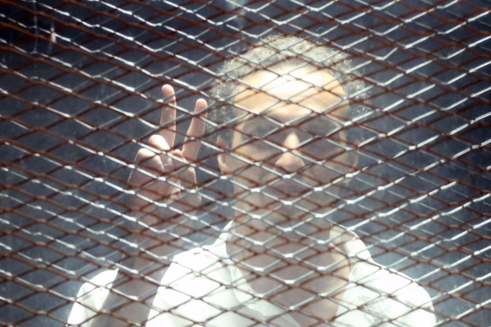 El fotoperiodista Mahmoud Abu Zeid, también conocido como 'Shawkan', hace la señal de la victoria dentro de la jaula desde la que siguió el juicio.