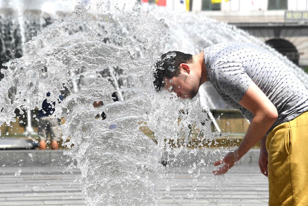 Un hombre se refresca en los chorros de agua de una fuente de la plaza De Ferrari en Génova, Italia.