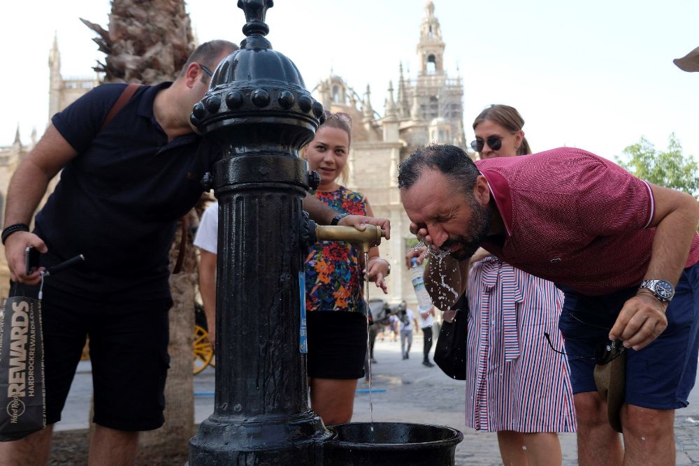 Varias personas se refrescan en una fuente esta tarde en Sevilla.