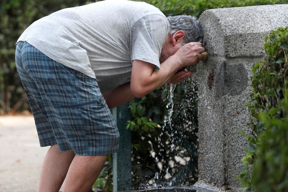 Un hombre se refresca en una fuente de un parque de Madrid.