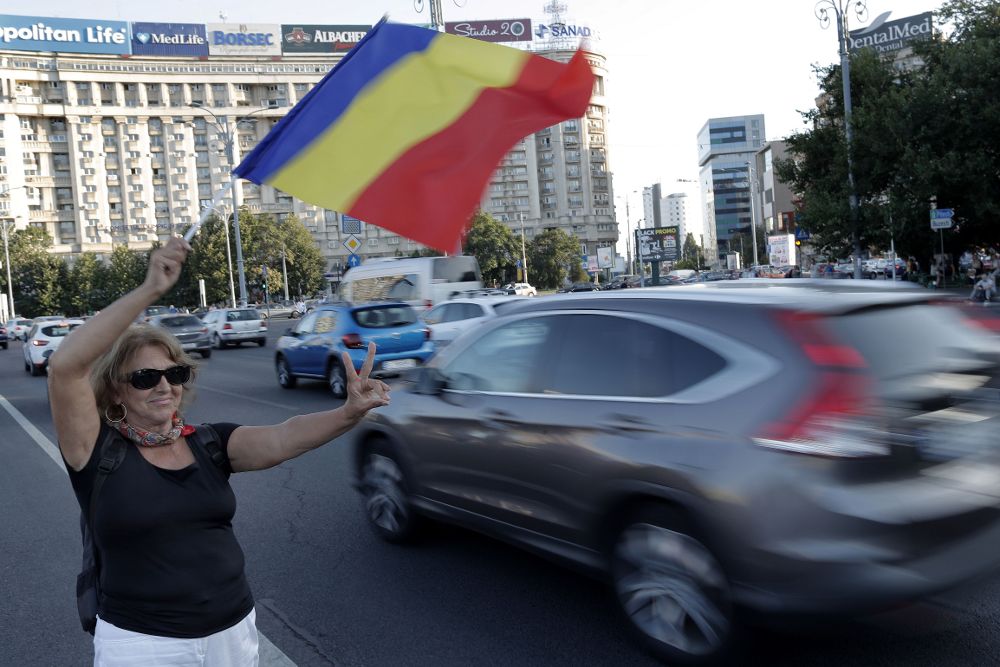 Una mujer agita la bandera nacional mientras hace señales de victoria a los vehículos que pasan durante el cuarto día de protesta anticorrupción contra el gobierno izquierdista, frente a la sede del gobierno en Bucarest, Rumanía.
